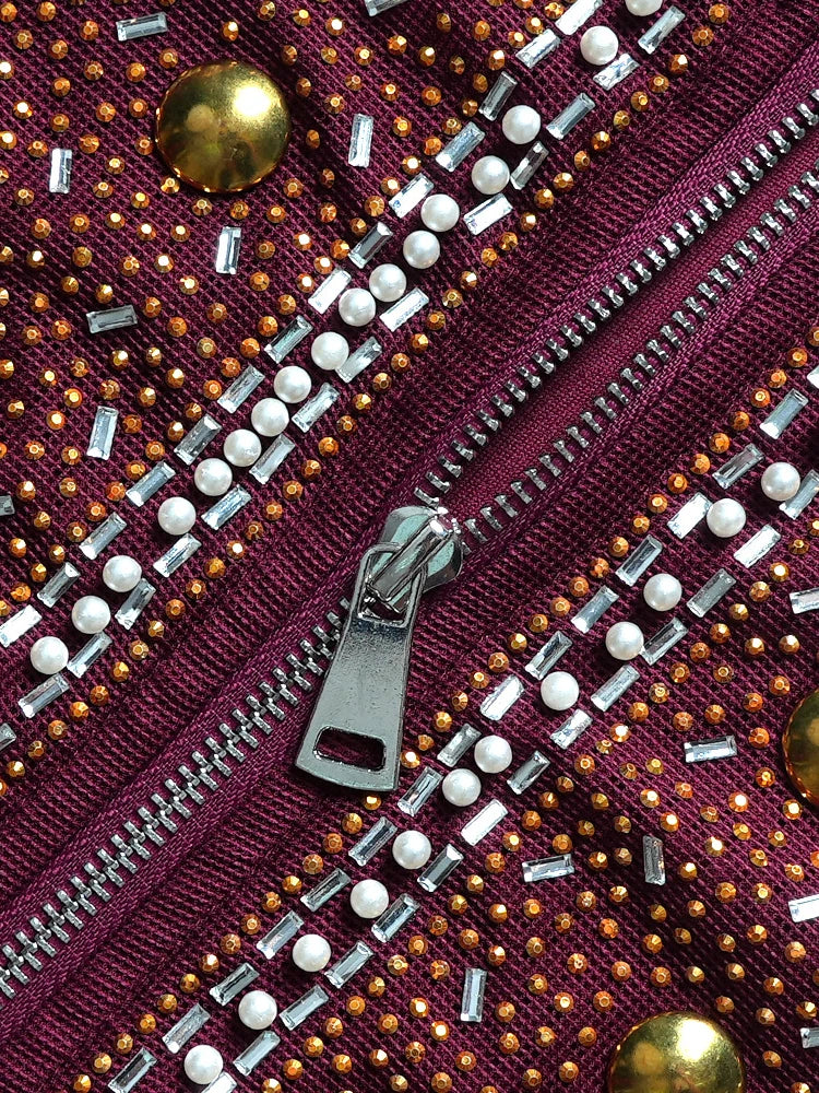 A close-up of a maroon garment featuring a silver zipper, white pearls, and gold embellishments.