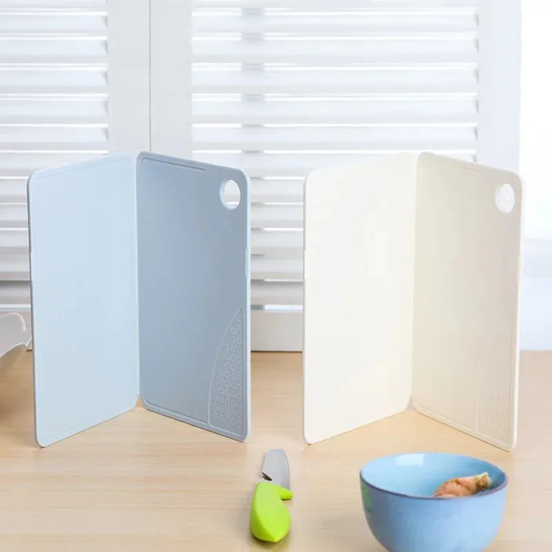 Showlu Smart General collapsible cutting board folded with a knife and vegetables ready for chopping on a clean kitchen surface.