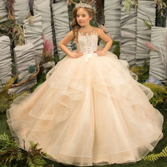 A girl wears a light champagne floor-length ball gown with floral appliques and tiered tulle ruffles.
