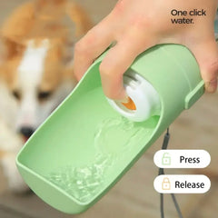 A hand holds a light green portable pet water bottle with a built-in drinking trough.