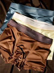 Three pairs of men's ice silk boxer shorts in blue, cream, and brown stacked on a brown surface.
