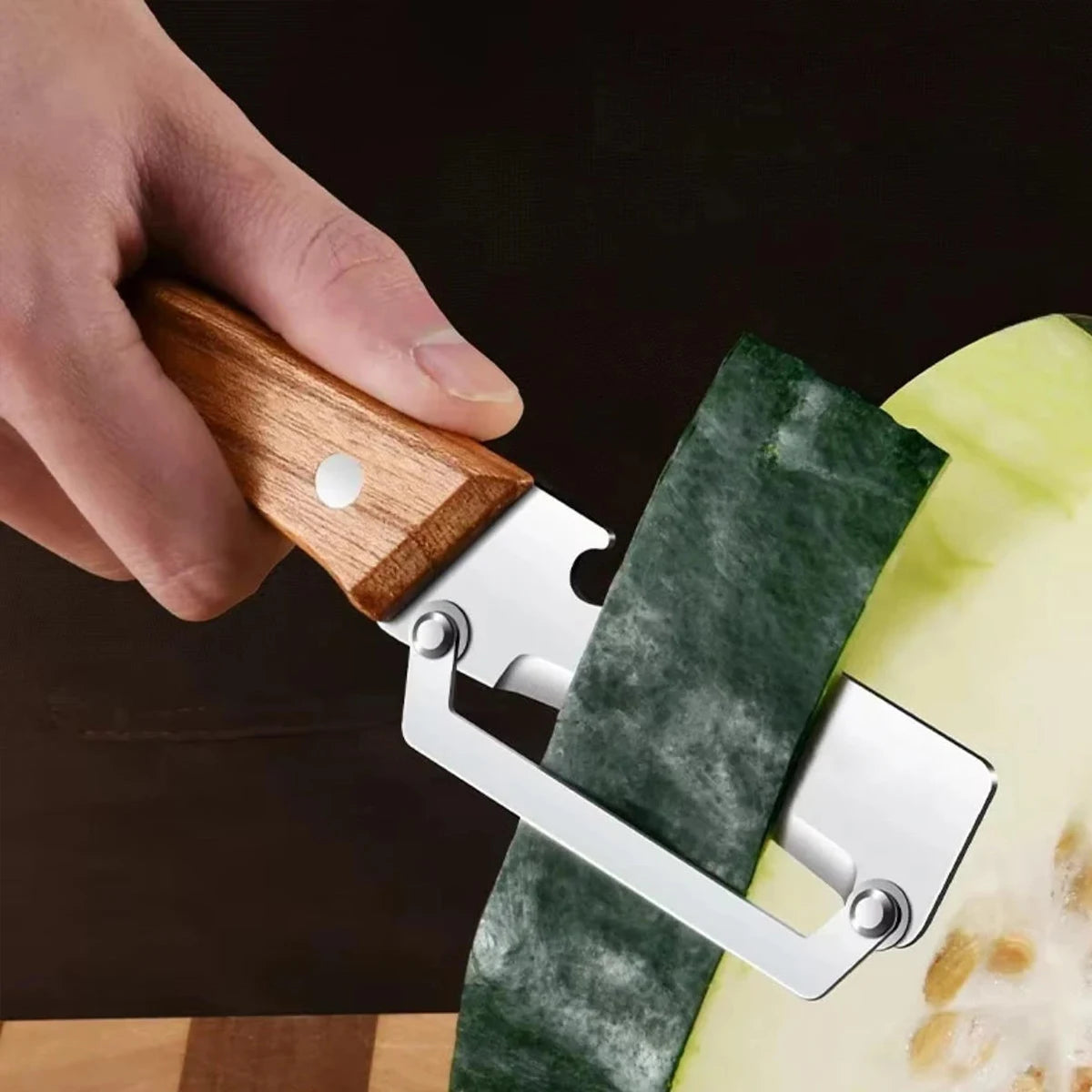 Stainless steel peeler with wooden handle for peeling and slicing fruits and vegetables, showing the durable kitchen tool in use