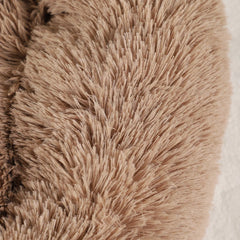 A close-up view of a soft, light brown faux fur pet bed with a plush, shaggy texture.