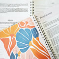 Spiral-bound women's Bible in a Year devotional journal with 52 weekly entries, featuring inspirational religious content.