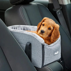 A small puppy sits inside a grey, plush-lined portable pet car seat on a vehicle armrest.