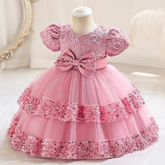 A pink short-sleeve party dress for girls featuring a lace bodice, a large bow, and sequin tiers.