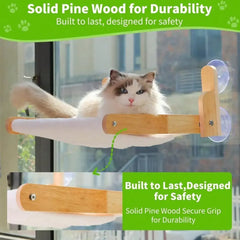 A cat rests on a wooden window perch featuring a soft hammock bed and suction cup mounts.