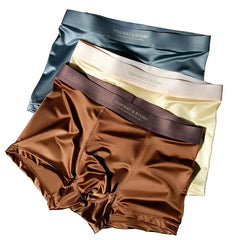 Three pairs of satin ice silk boxer shorts in blue, cream, and brown stacked on each other.