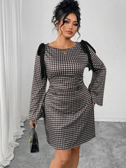 A woman wears a long-sleeved, knee-length black and white gingham dress with shoulder tie details.