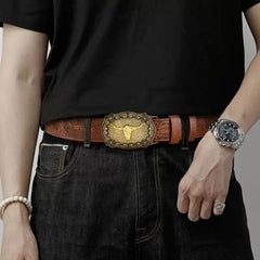 A person wears a brown embossed PU leather belt featuring a gold-toned bull head buckle.