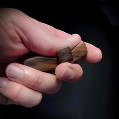 A hand holds a small, smooth, dark wooden pocket cross designed for tactile comfort.