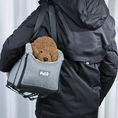 A person carries a small brown dog in a grey portable pet car seat carrier.