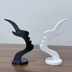 Two minimalist 3D-printed side profile sculptures in black and white stand on a wooden surface.