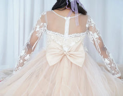 A girl wears a long-sleeved floral lace ball gown with a large bow on the back.