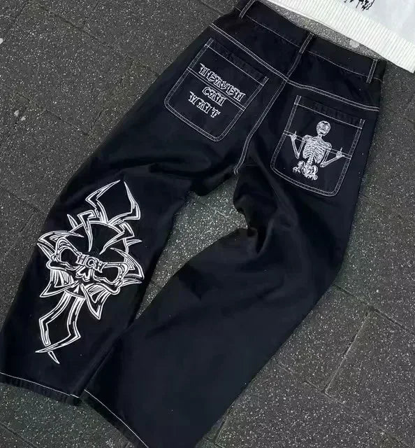 Blue low-rise flared denim jeans with rhinestone wing embroidery, studded pockets, and streetwear style from American Vintage Y2K collection.