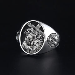 A silver ring featuring an embossed image of Jesus carrying a cross and a sacred heart emblem.