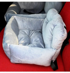 A light blue plush pet car seat with high cushioned walls sitting on a red vehicle seat.