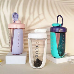 Three protein shaker bottles in pastel pink, white, and teal stand on white display blocks.