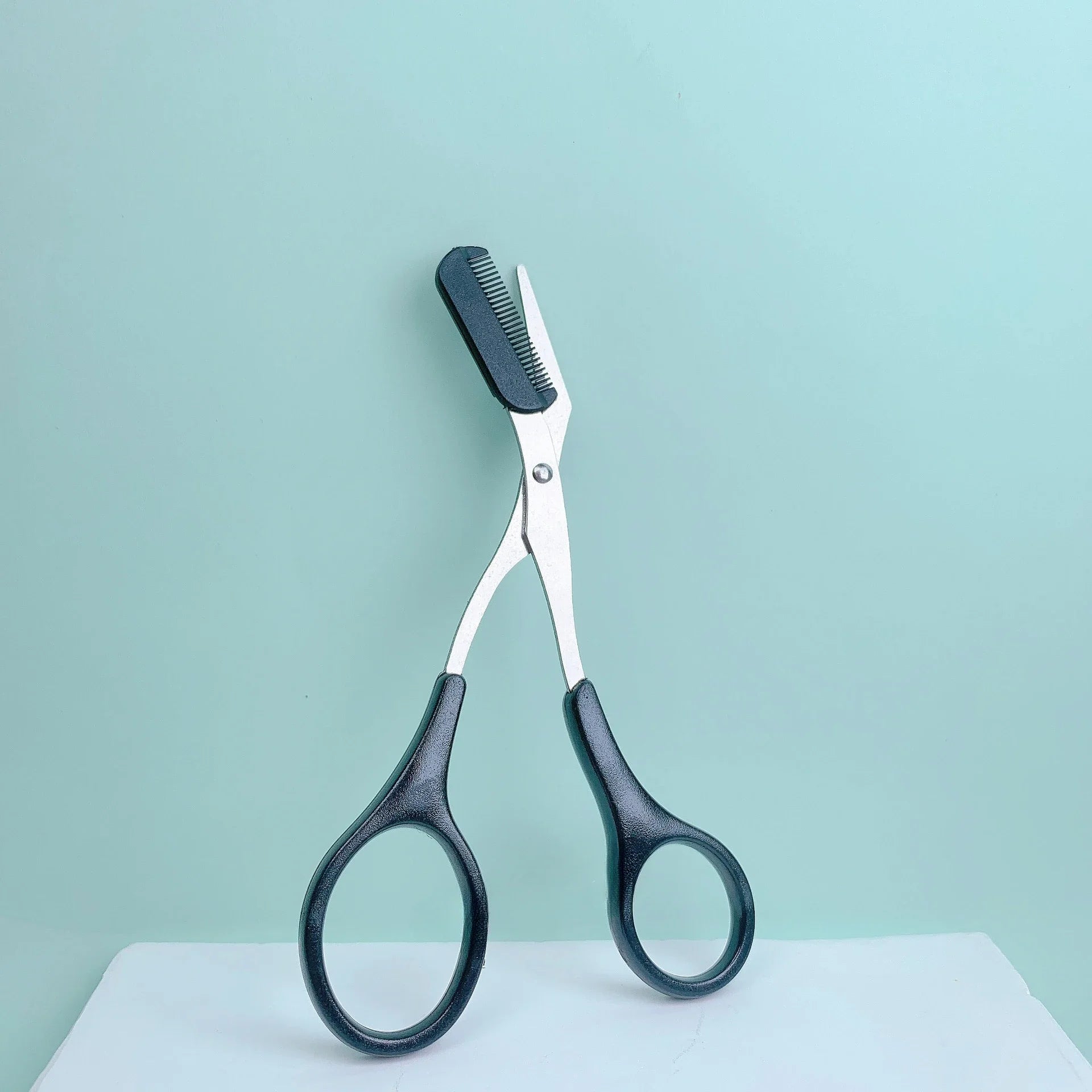 Pink stainless steel eyebrow trimming scissors with built-in comb for precise grooming and shaping of eyebrows.