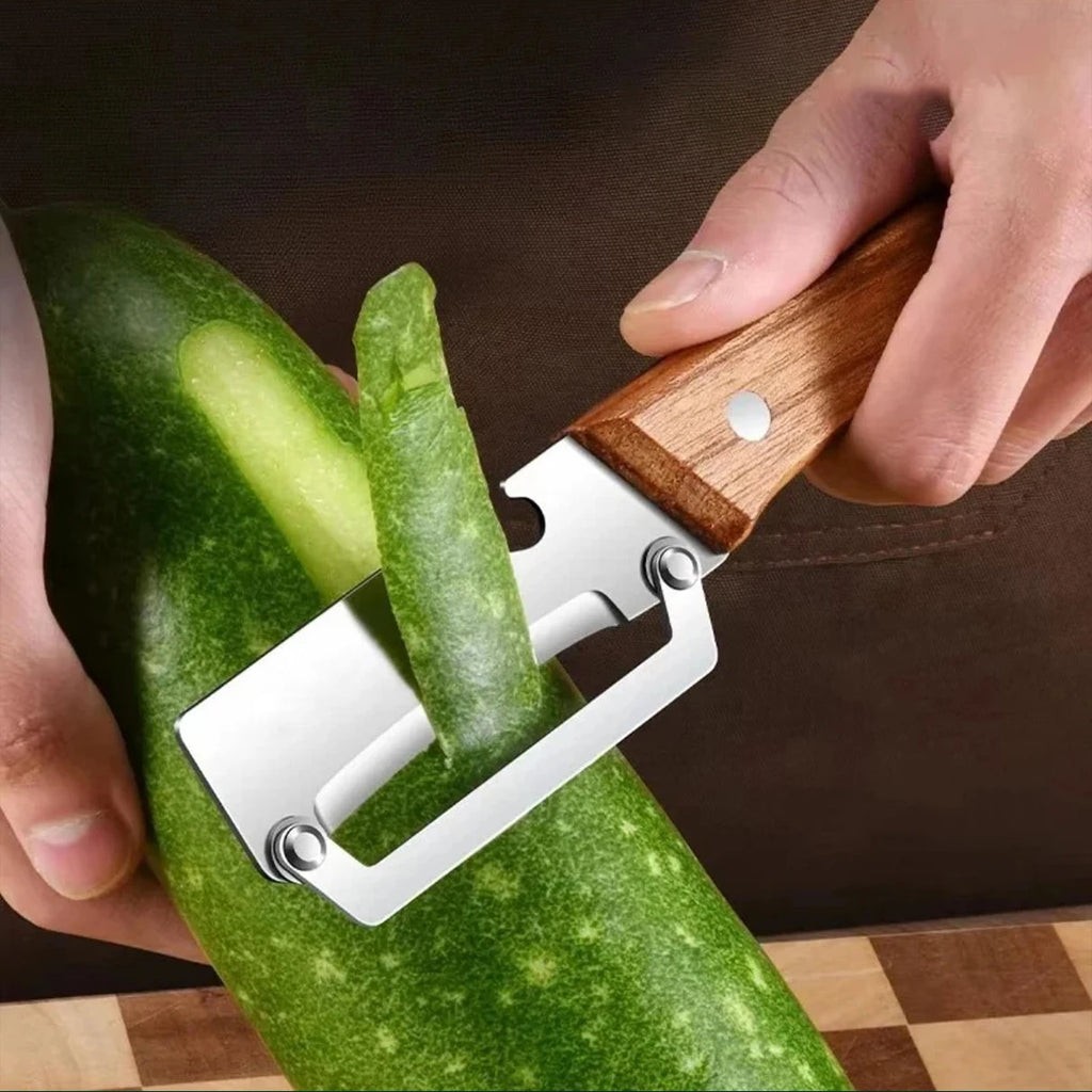Stainless steel peeler with wooden handle for peeling and slicing fruits and vegetables, showing a close-up of the tool in use.