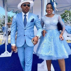 A man wearing a sky blue two-button suit with a white hat and sunglasses stands next to a woman.