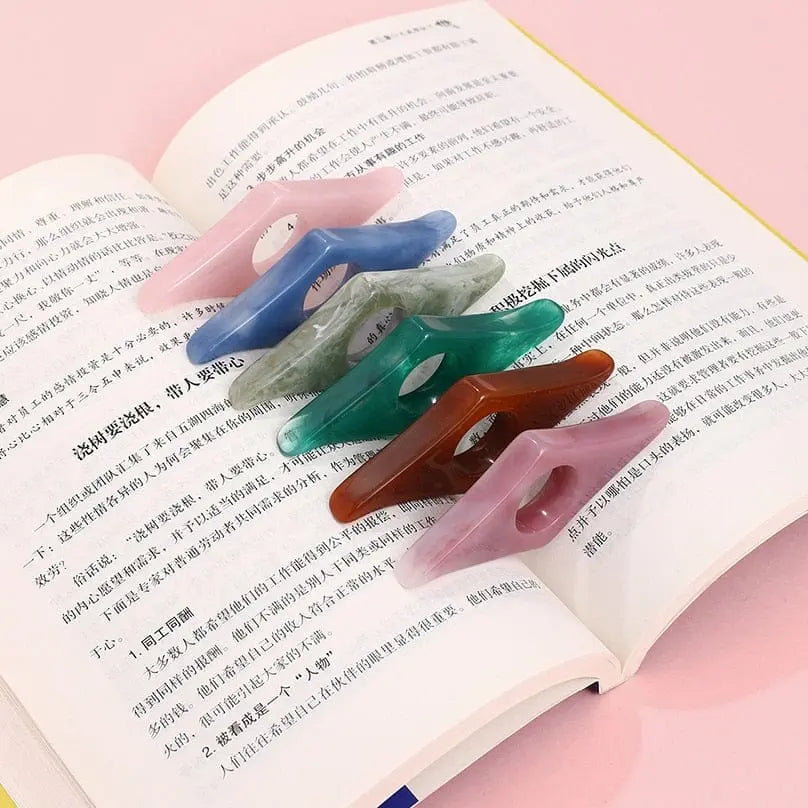 Five Thumb Book Support Page Holders, ideal as reading aids or bookmarks, are arranged in a row on an open book with Chinese text. The soft pink background highlights these convenient school supply accessories.