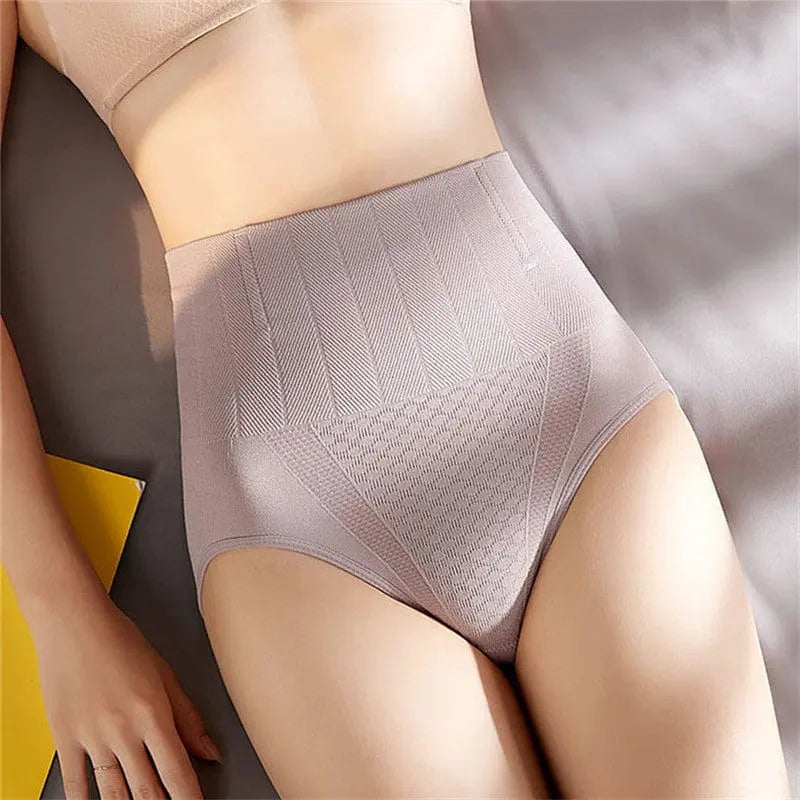 A woman wearing Underwear Bragas Fajas Women Shaper Thong Bodyshaper in nude high waist shapewear lies on a bed, showing her midsection and upper thighs with a yellow object nearby.