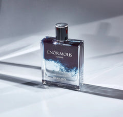 A rectangular glass bottle of Enormous Homme eau de toilette with a dark blue and clear liquid.