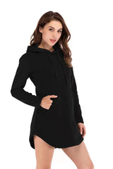 Woman models a black Showlu cotton sports hoodie dress with long sleeves, hood, and front pocket against a white background.