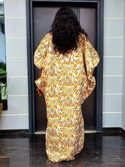 A woman wears a loose-fitting, floor-length satin caftan featuring a gold fan-patterned sequin design.