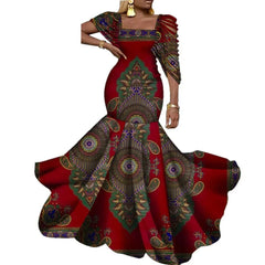 A woman wears a red, floor-length mermaid dress featuring a vibrant green and gold wax print.