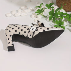 A cream-colored pointed-toe pump with black polka dots, a bow detail, and a chunky block heel.