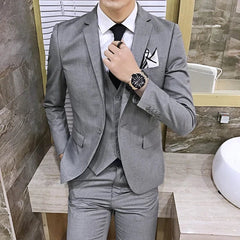 A man wears a slim-fit grey three-piece suit with a white shirt and black tie.