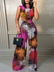 A woman wears a sleeveless, wide-leg jumpsuit featuring a vibrant, multi-colored abstract print.