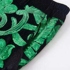 Close-up of black velvet trousers featuring intricate green sequin floral patterns.