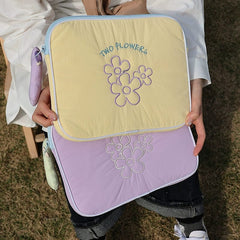 A person holds a yellow and a purple quilted tablet bag, each featuring embroidered flower designs.