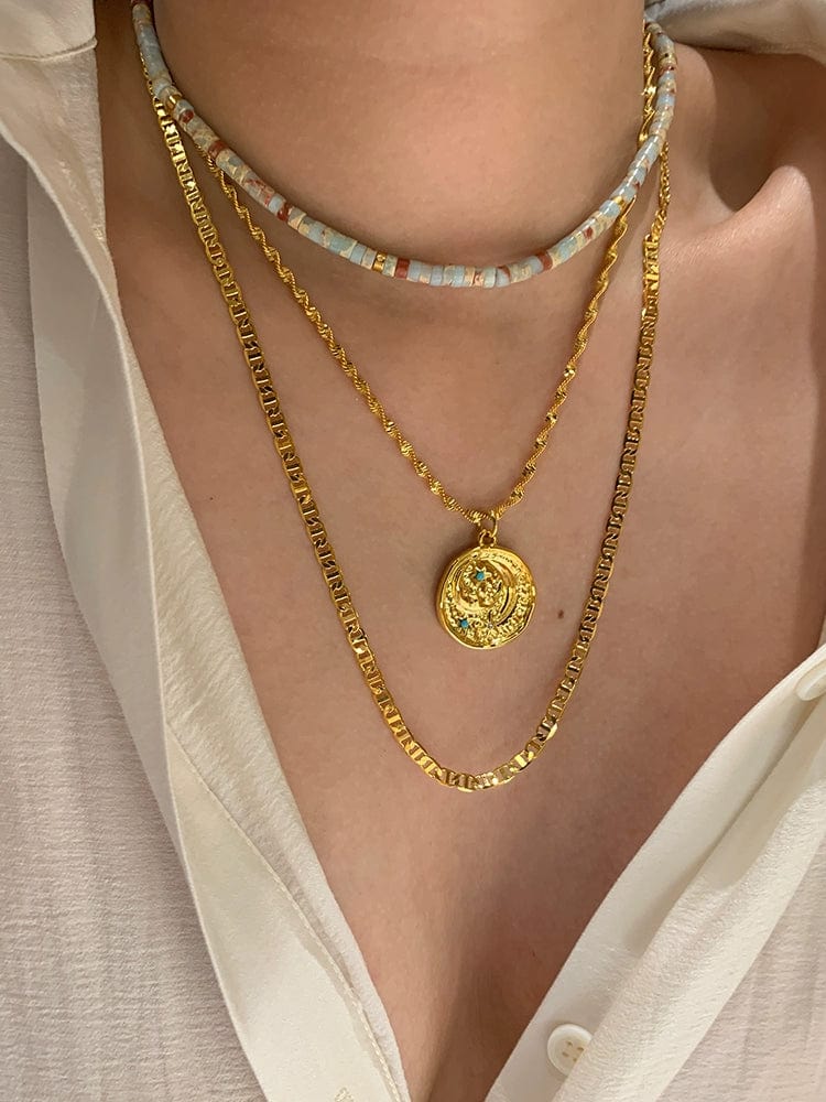 Turquoise star and moon pendant necklace featuring vintage gold coin brass design, worn on a woman's twin clavicle chain.