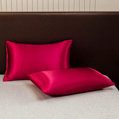 Two vibrant magenta satin pillowcases rest on a light gray bed against a dark brown headboard.