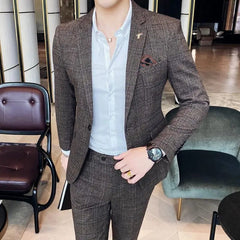 A man wears a brown plaid two-piece suit with a white button-down shirt and a lapel pin.