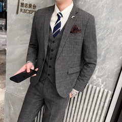 A man wears a grey plaid three-piece suit with a white shirt, blue tie, and brown pocket square.