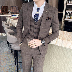 A man wears a brown plaid three-piece suit with a white shirt and a navy striped tie.
