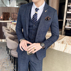A man wears a navy blue plaid three-piece suit with a white shirt and striped tie.