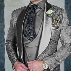 A man wears a grey three-piece jacquard suit with a paisley tie, white boutonniere, and gold watch.
