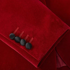 A close-up of a red velvet blazer sleeve featuring four black fabric-covered buttons.