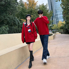 A young couple walks outdoors wearing matching red long-sleeved pullover sweaters.