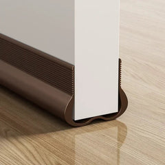 A brown flexible PVC door bottom sealing strip installed on the edge of a white door.