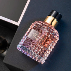 A glass perfume bottle with a textured diamond pattern and a gold cap sits on a dark surface.
