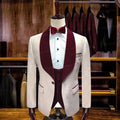 Pink men's slim fit 3-piece suit with burgundy velvet lapel, formal wedding or prom attire, featuring blazer, vest, and trousers.