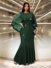 A woman wears a floor-length, dark green sequined evening gown with a matching sheer cape overlay.