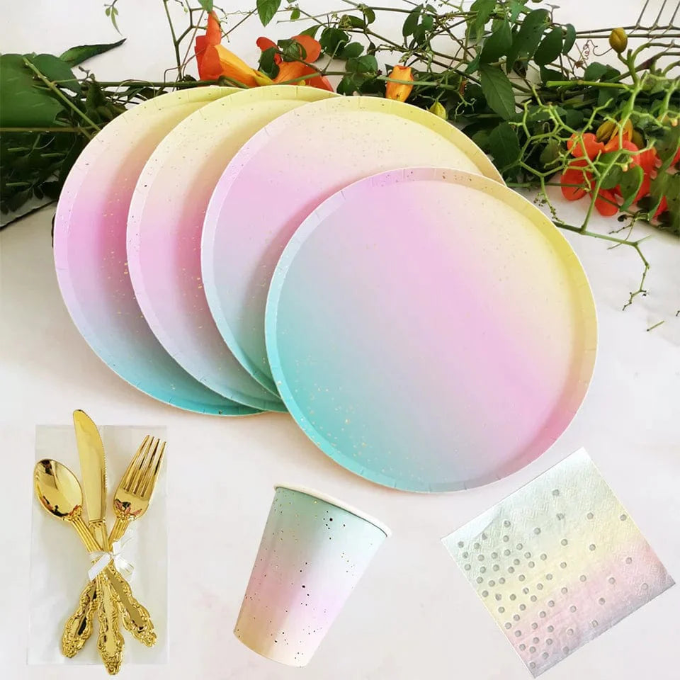 Rainbow birthday party tableware set with paper plates, napkins, cups, and tablecloth featuring colorful rainbow designs.
